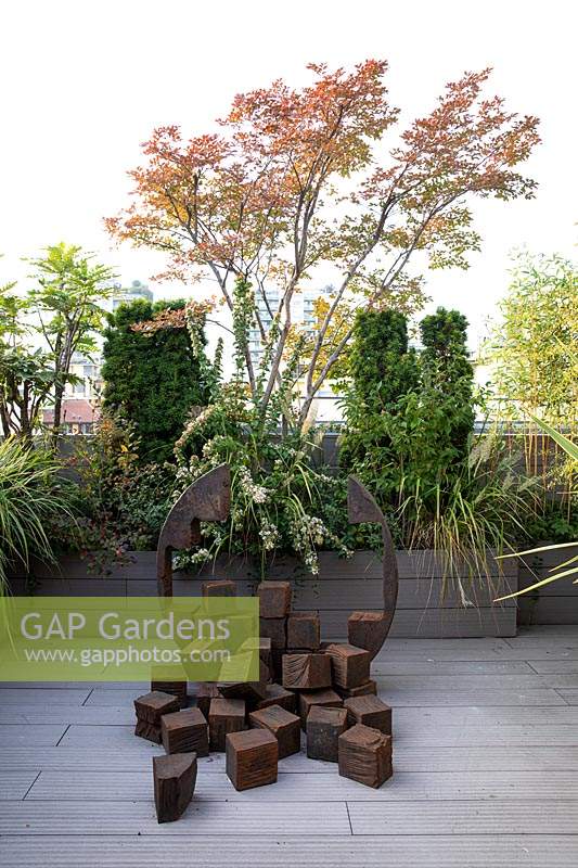 Decked roof garden with sculpture in front of planter of trees and shrubs 