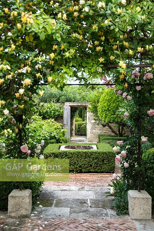 Archway in rose garden with view through to hedging and wall boundary with open doorway.