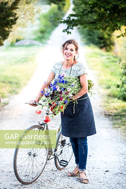 Woman standing with bicycle, holding bunch of just picked cut flowers 