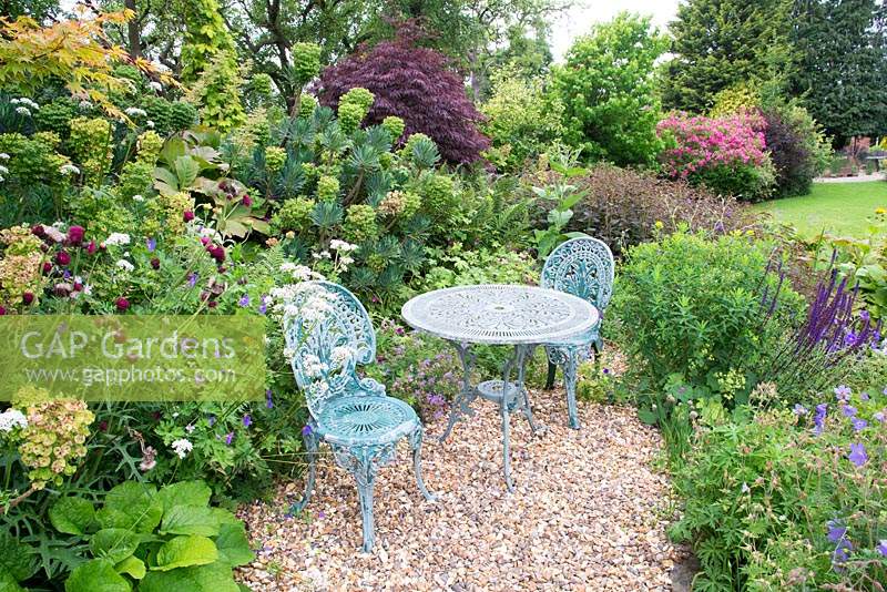 Table and chairs on gravel seating area surrounded by mixed borders 