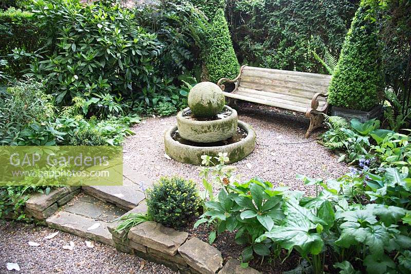 Shaded seating area in town garden, gravel with mixed beds and stone focal point