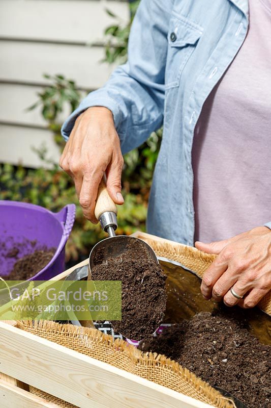 Woman using a metal scoop to add compost to a wooden crate