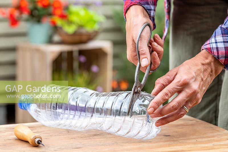 Using metal scissors to cut the base off a large plastic bottle