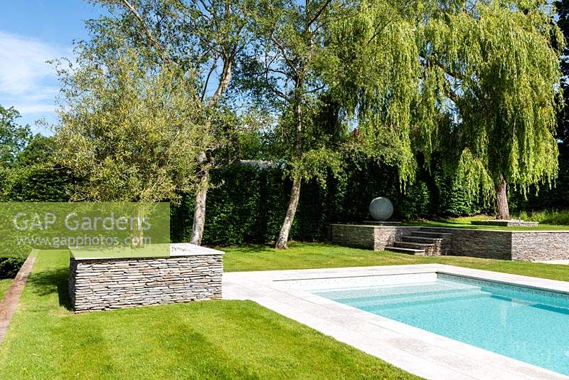 Modern garden with swimming pool and trees planted in raised beds edged with granite walls