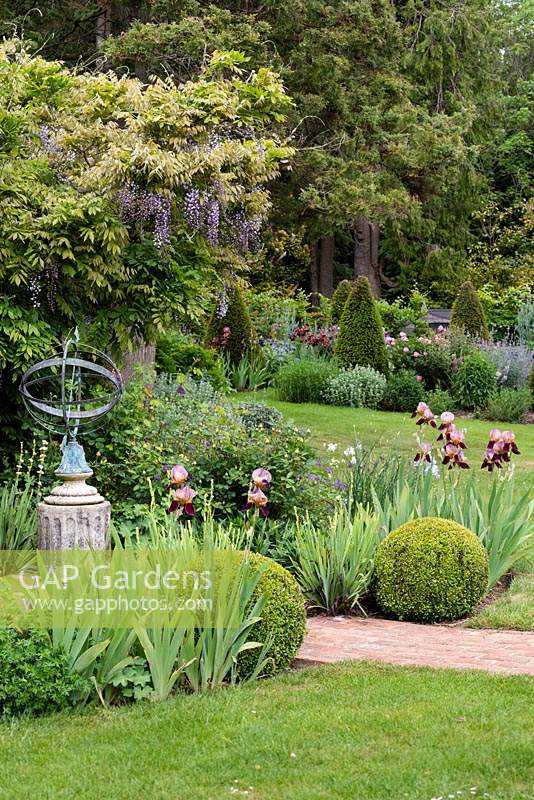 View across flower beds and Wisteria pergola with Armillary sphere towards the long border with topiary