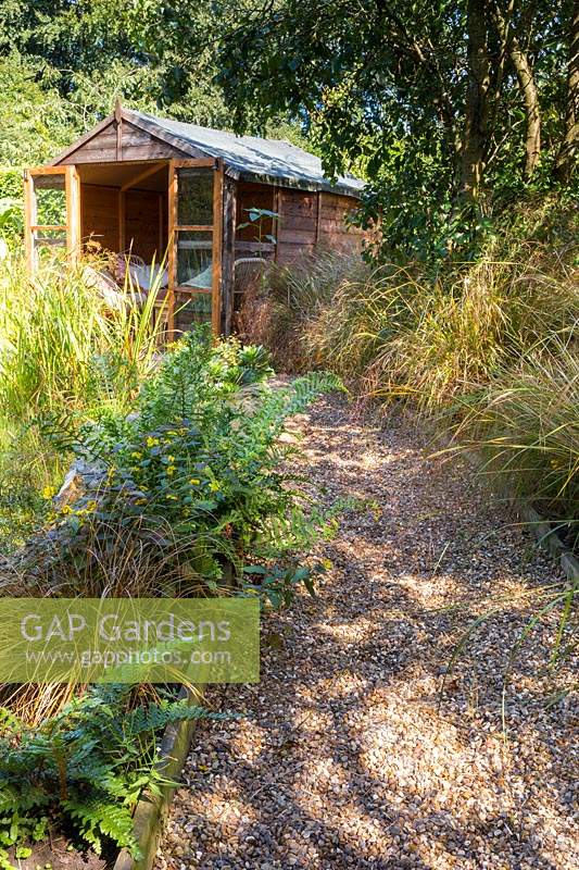 Pathway to the summerhouse, beds lined with various ferns, perennials and ornamental grasses including Stipa arundinacea