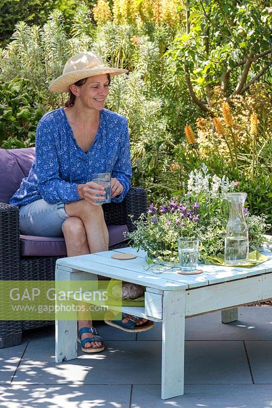 Woman relaxing with a glass water admiring the flowers in her table planter