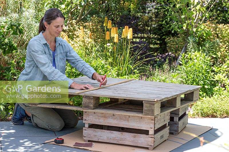 Woman using a piece of wood and a pencil to mark out a cutting line on a wooden pallet