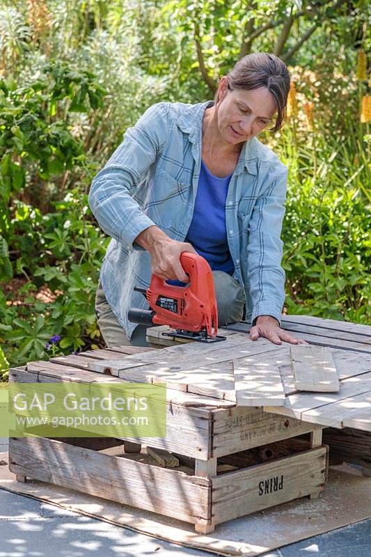 Woman cutting out wooden sections from an old wooden pallet. 