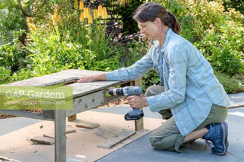 Woman using cordless electric screwdriver to attach side panels to pallet table. 