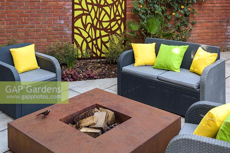 Small Modern Garden with sofa and armchairs and cushions around fire pit
