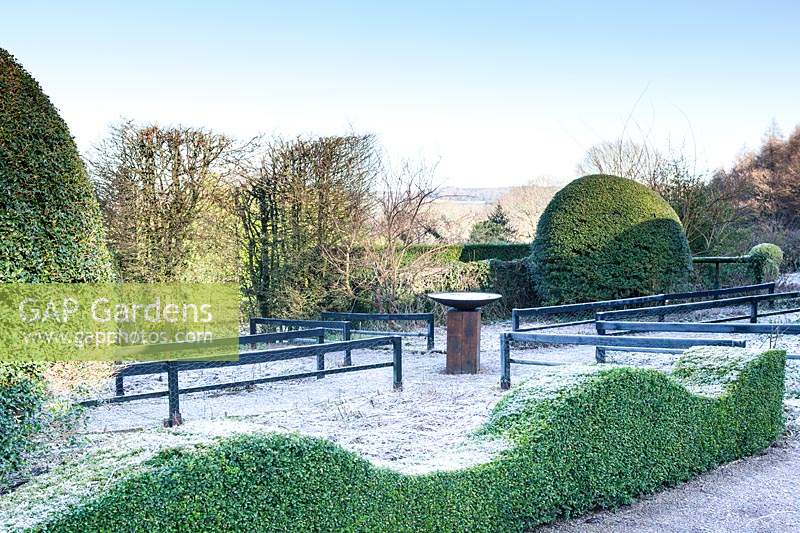 Front Garden with wave-form frosted hedge of Buxus, black painted wooden rails and bird bath. 
