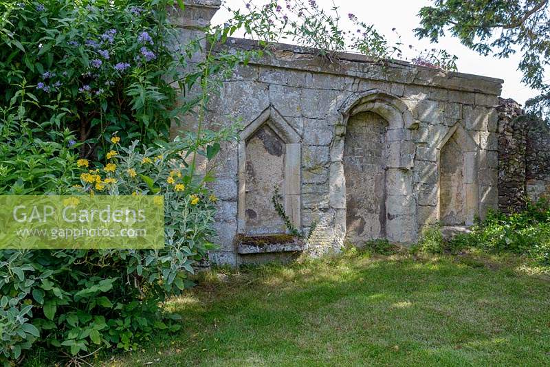 Stone ruins from a church yard in the garden, informal planting of shrubs nearby
