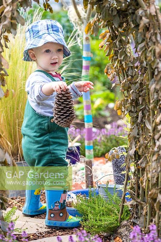 Young toddler holding a pine cone in sensory garden