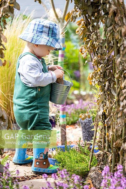 Young toddler putting items into a metal bucket in sensory garden