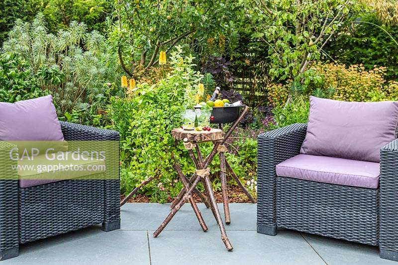 Trio of tripod structures - a planter with planted with mints, a small table holding drinks, and a drinks cooler on a slate patio with garden furniture 