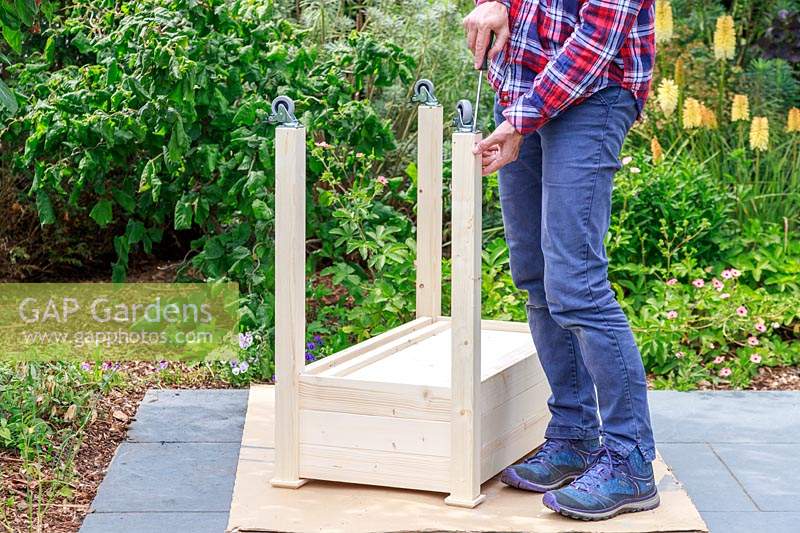 Woman using a screwdriver to attach small casters to the legs of a raised wooden planter