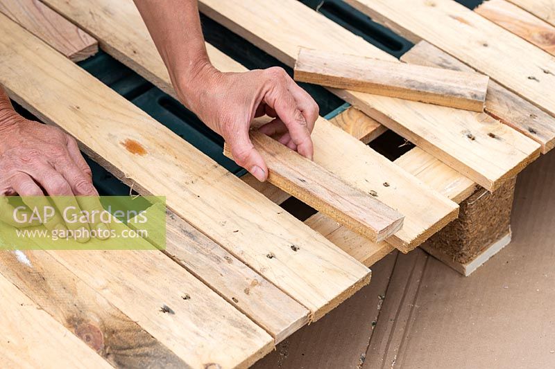 Woman fitting cut pieces of narrow wood to fill gaps in pallet. 