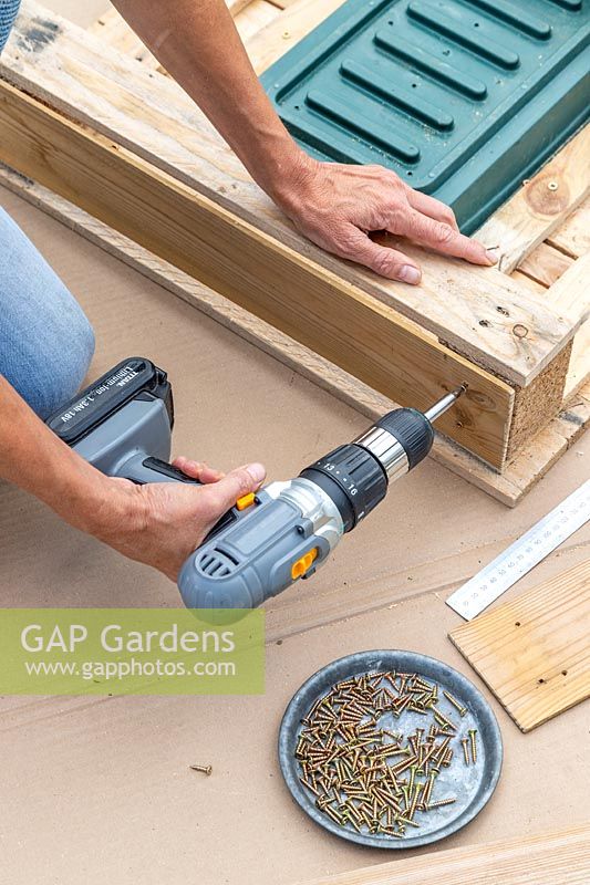 Woman using an electric screwdriver to fix planks on to the sides of the pallet to hide the planting tray. 
