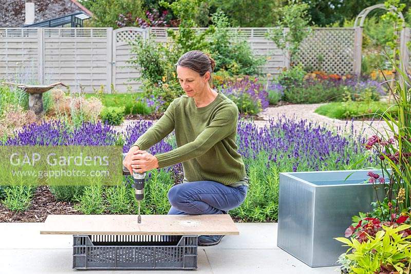 Woman using cordless electric drill to create drainage holes in wooden base for planter