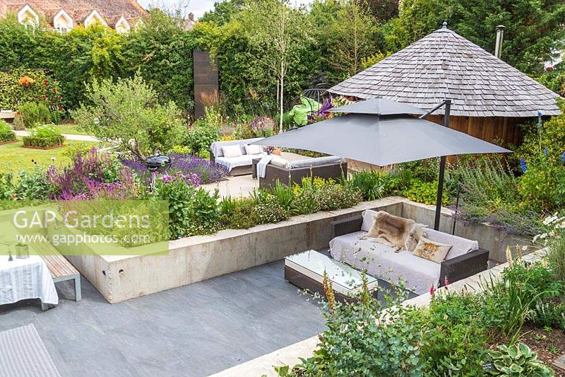 Sunken garden with lounge furniture and parasol and view to patio by hut 