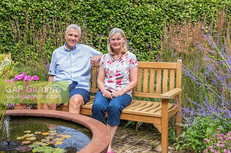Garden owners sat on bench by corten steel water feature