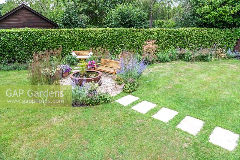 View from above of suburban garden with lawn and a circular bed with paved seating area and water feature
