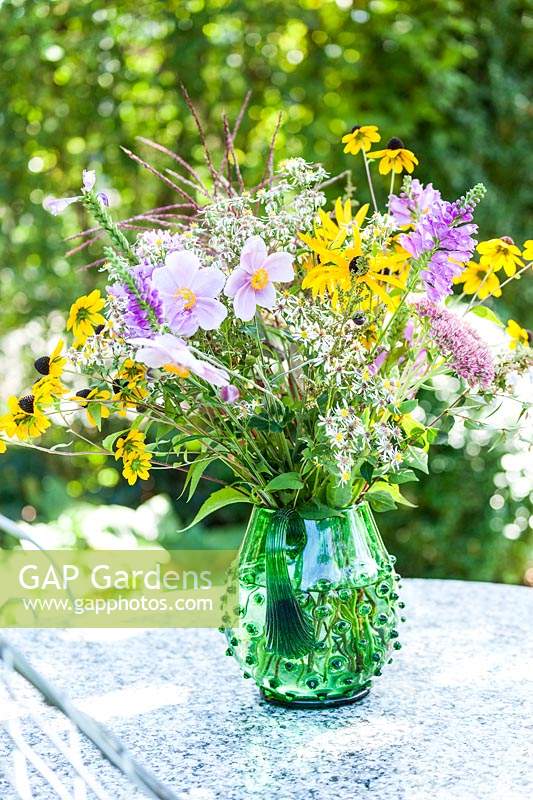 Vase with Rudbeckia, Aster, Anemone and grasses on garden table in September