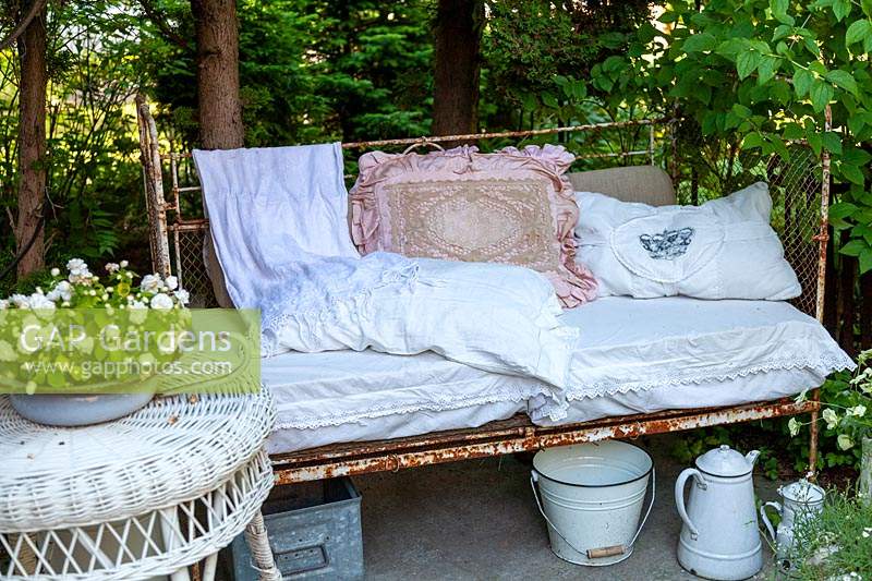Old bed frame as a bench, pillows and a wicker table in the foreground
