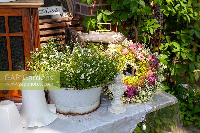 Large metal bowl container next to floral wreath and collectables on table 