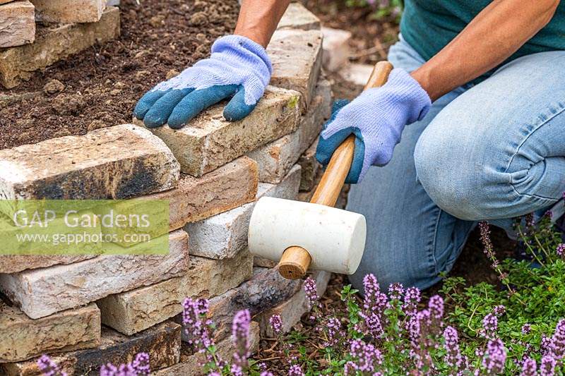 Woman using a rubber mallet to adjust the position of some bricks to ensure a nice round shape