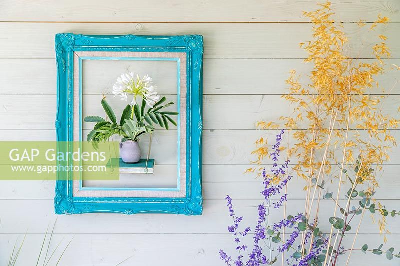 Framed shelf with display of vase with Melianthus foliage and white Agapanthus flowers