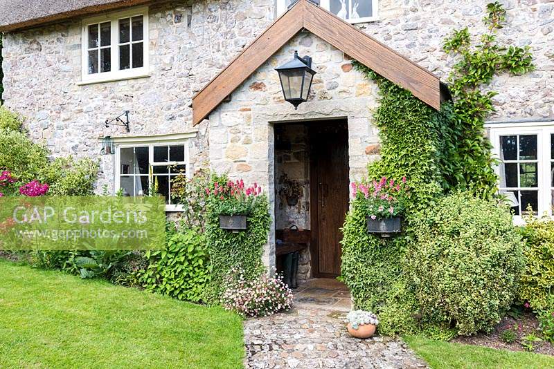 Farmhouse front door framed by wall pots of pink diascias and ivy 