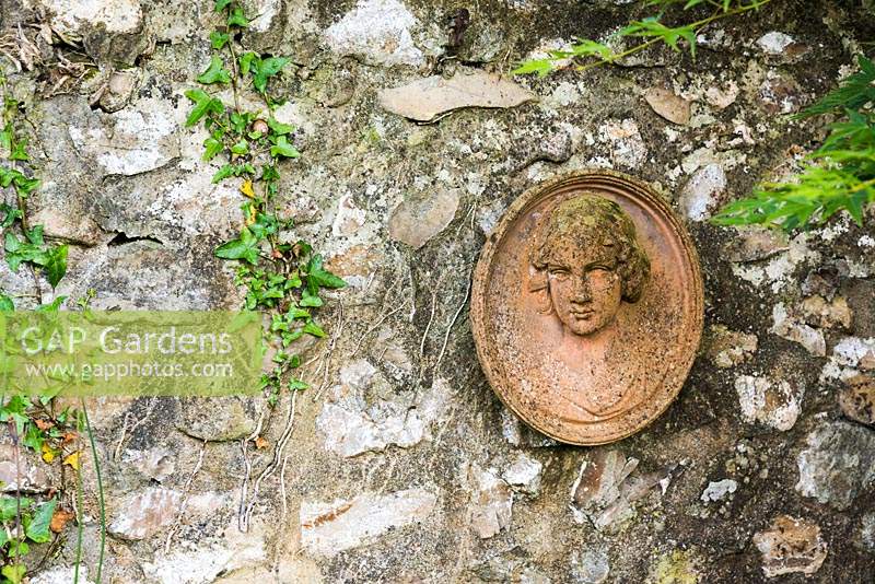 Terracotta roudel of a woman's head on a stone wall with ivy 