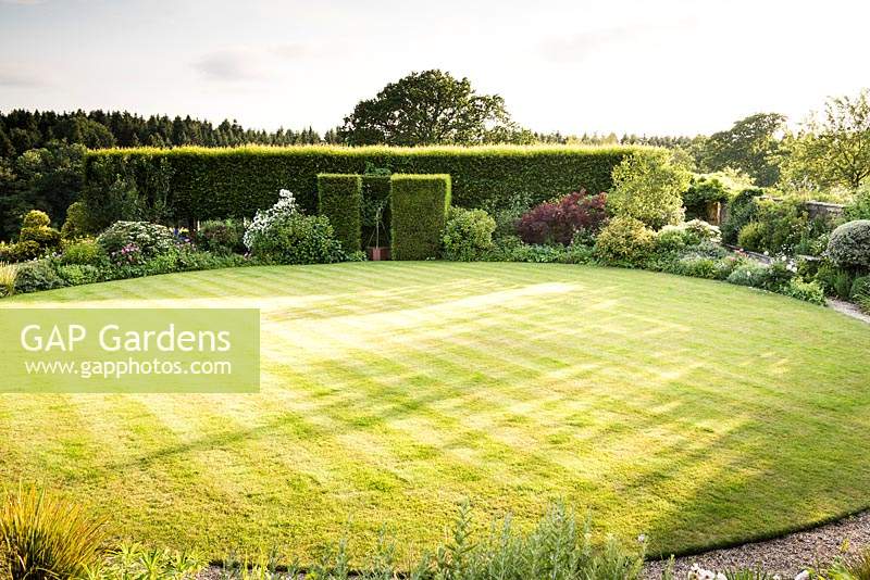 Circular lawn surrounded by borders of shrubs and perennials,