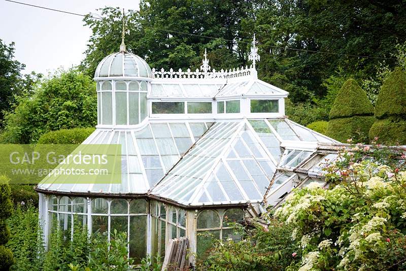 Rare Mackenzie and Moncur glasshouse surrounded by clipped evergreens and lush planting in the walled garden 