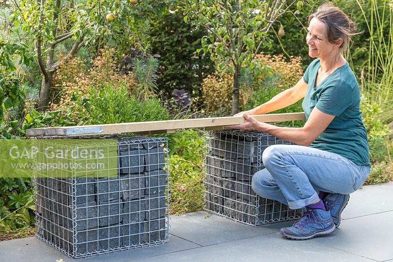 Woman placing seat made of two scaffolding boards on top of granite filled gabions.