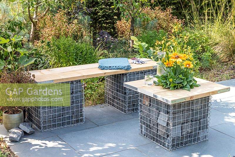 Gabion and scaffolding board bench and table on slate patio in modern garden. 