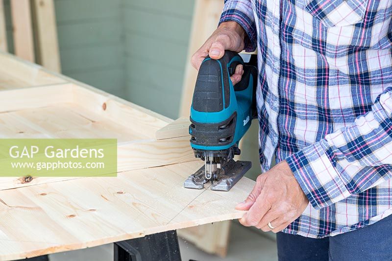 Using a cordless jigsaw to cut roof shape in shed back panel
