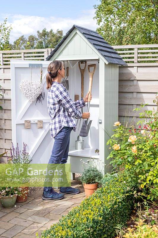 Woman placing a spade inside mini wooden garden shed