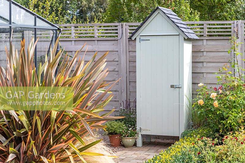 Mini garden shed fitted with a door on path next to wooden fence