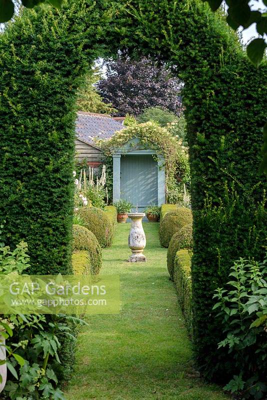 View through Taxus baccata - Yew arch to The Secret Garden with Sundial and clipped Buxus - box hedges and balls. 