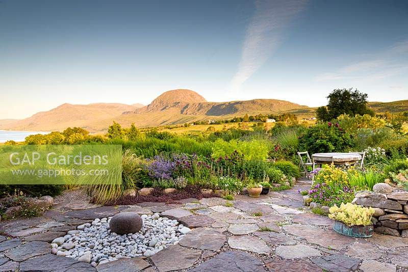 View over Scottish garden and seating area with rustic wooden table. 