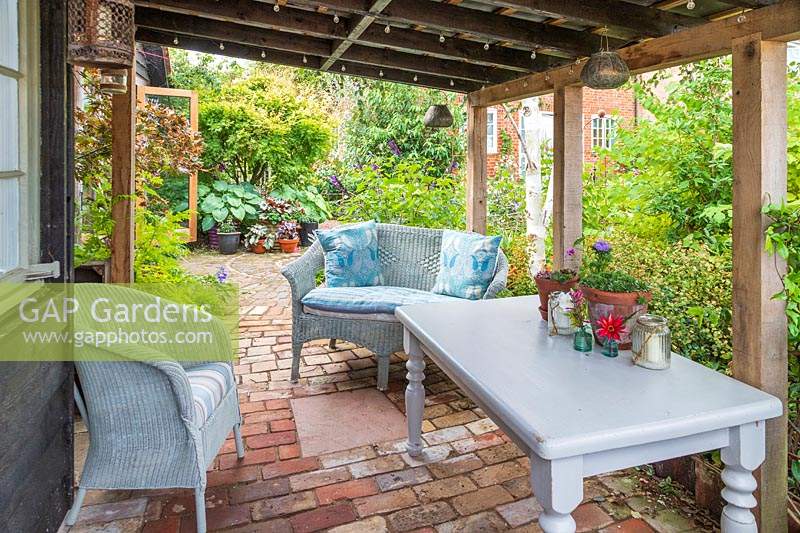 Wicker furniture on veranda with brick paving and view to garden