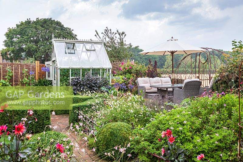 Country garden with wooden greenhouse and seating area under parasol