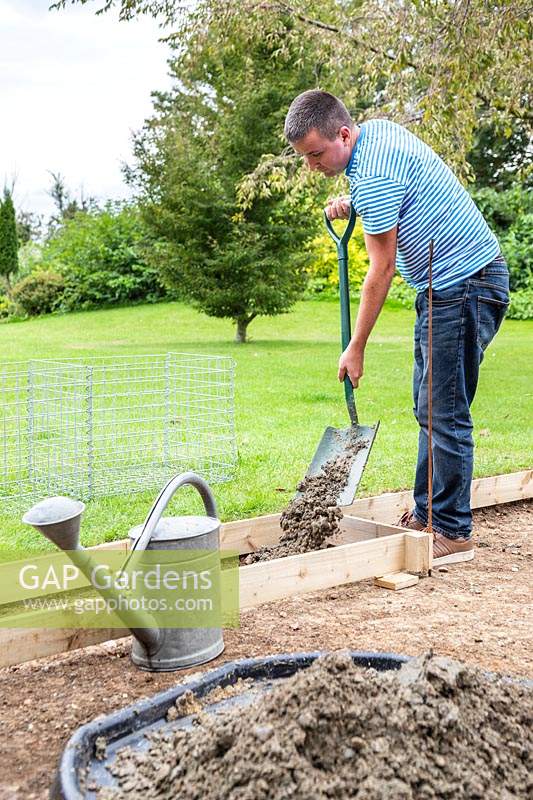 Man shoveling concrete mix into wooden frame to create the base for the gabions