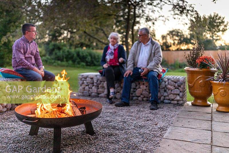 Lit firepit with people sitting on gabion benches 