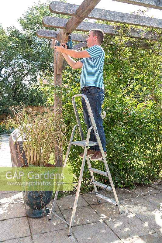 Man on a ladder using an electril drill to predrill a fine hole 