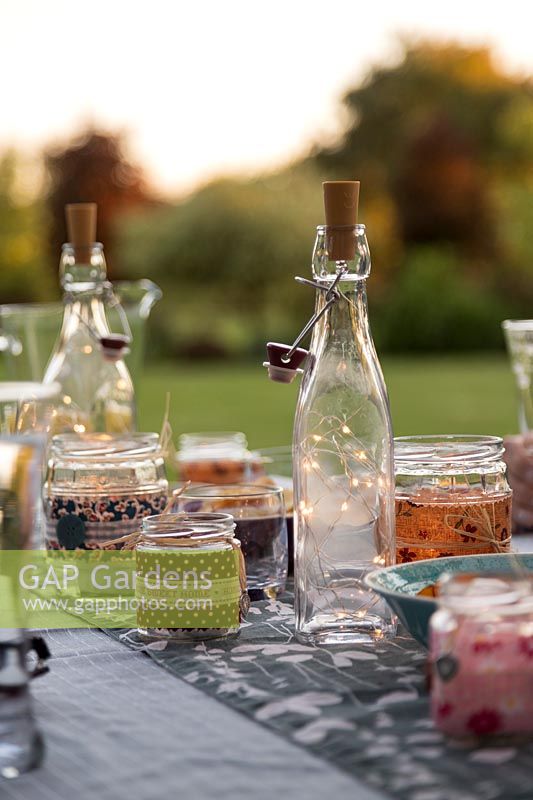 Glass bottles with light chains inside used as table decoration for evening garden party