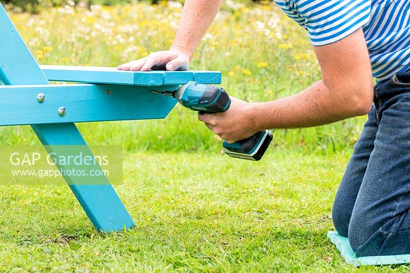 Man using an electric screwdriver to fix seat to bench